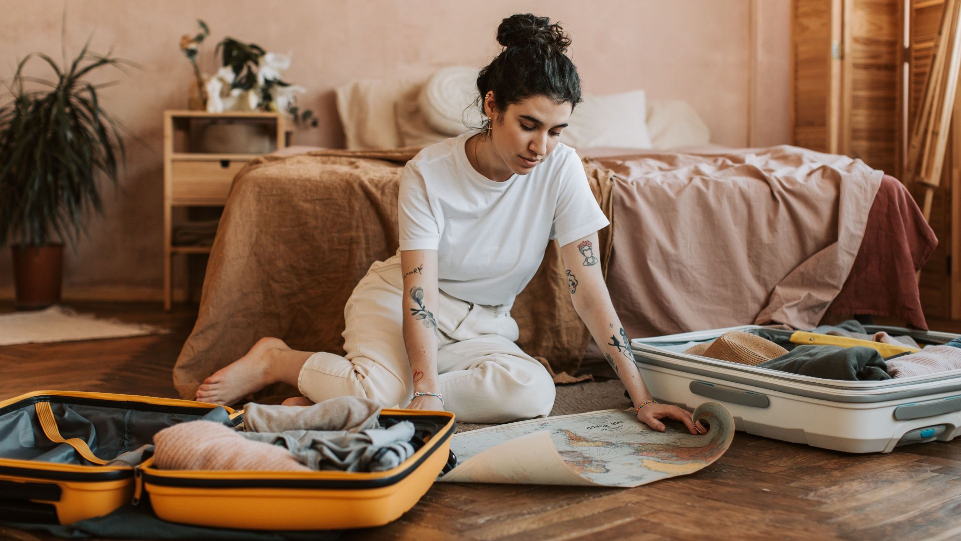Young woman preparing for a trip, packing suitcases in a cozy bedroom setting.