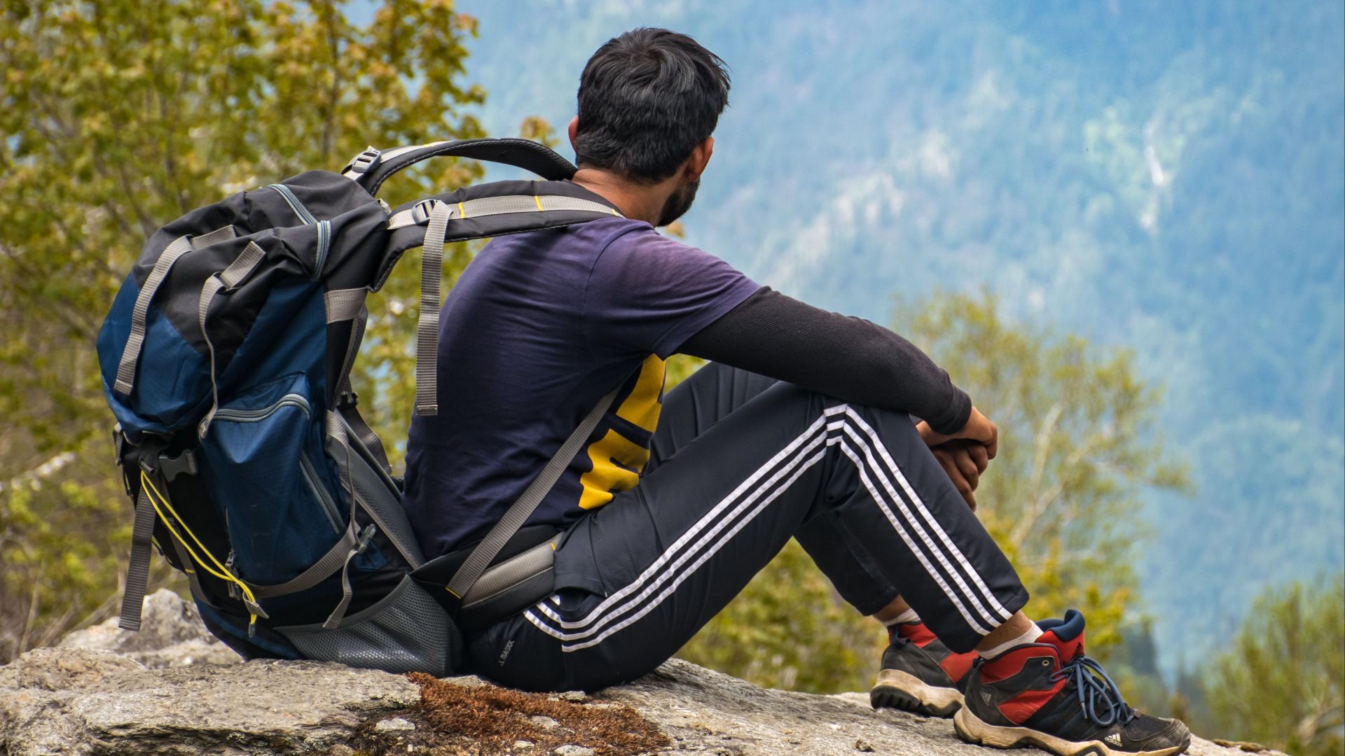 A hiker rests on a rock, taking in a stunning mountain landscape under a clear sky.