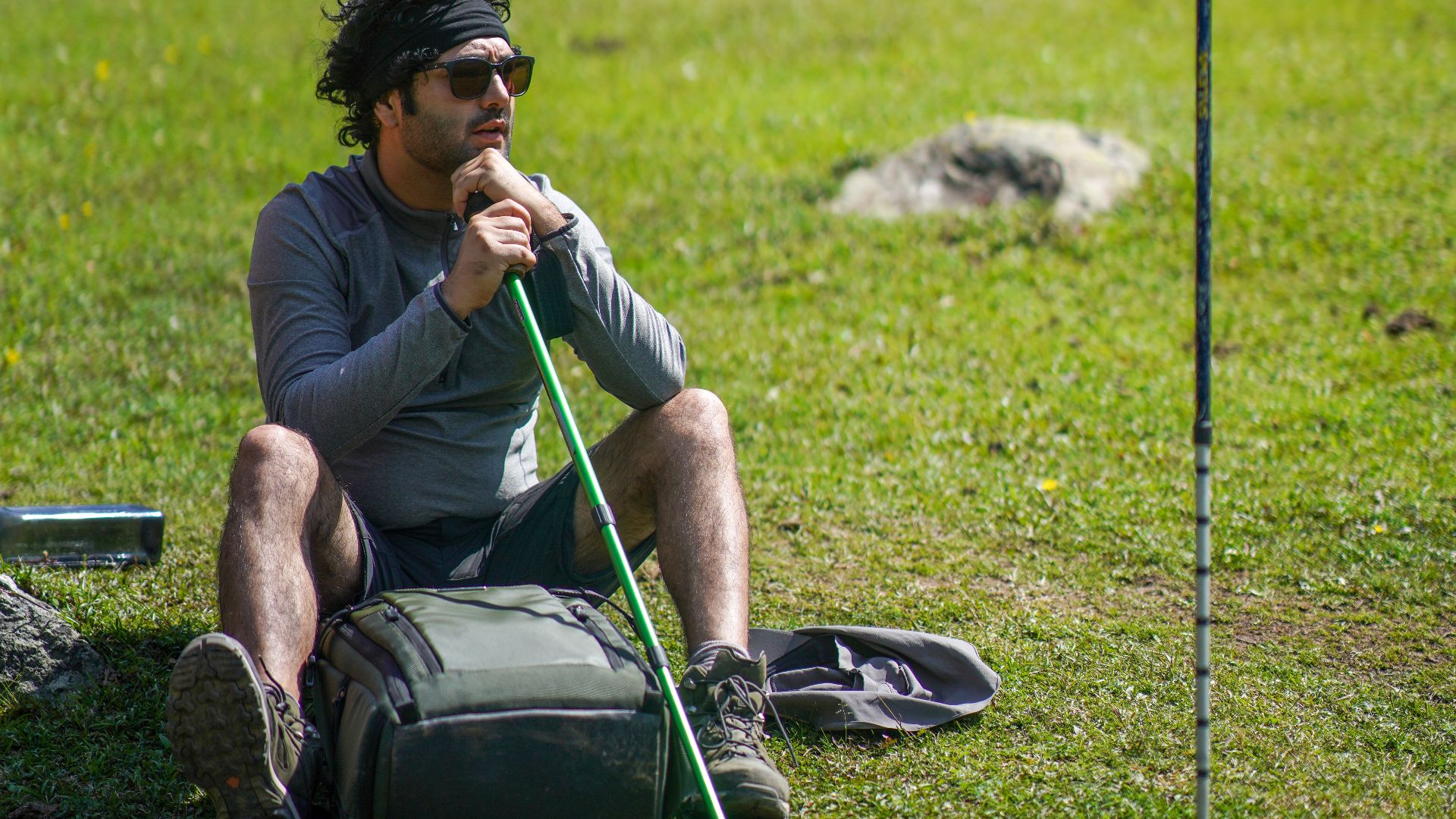 A hiker takes a rest in a green forest landscape with trekking poles and a backpack nearby.