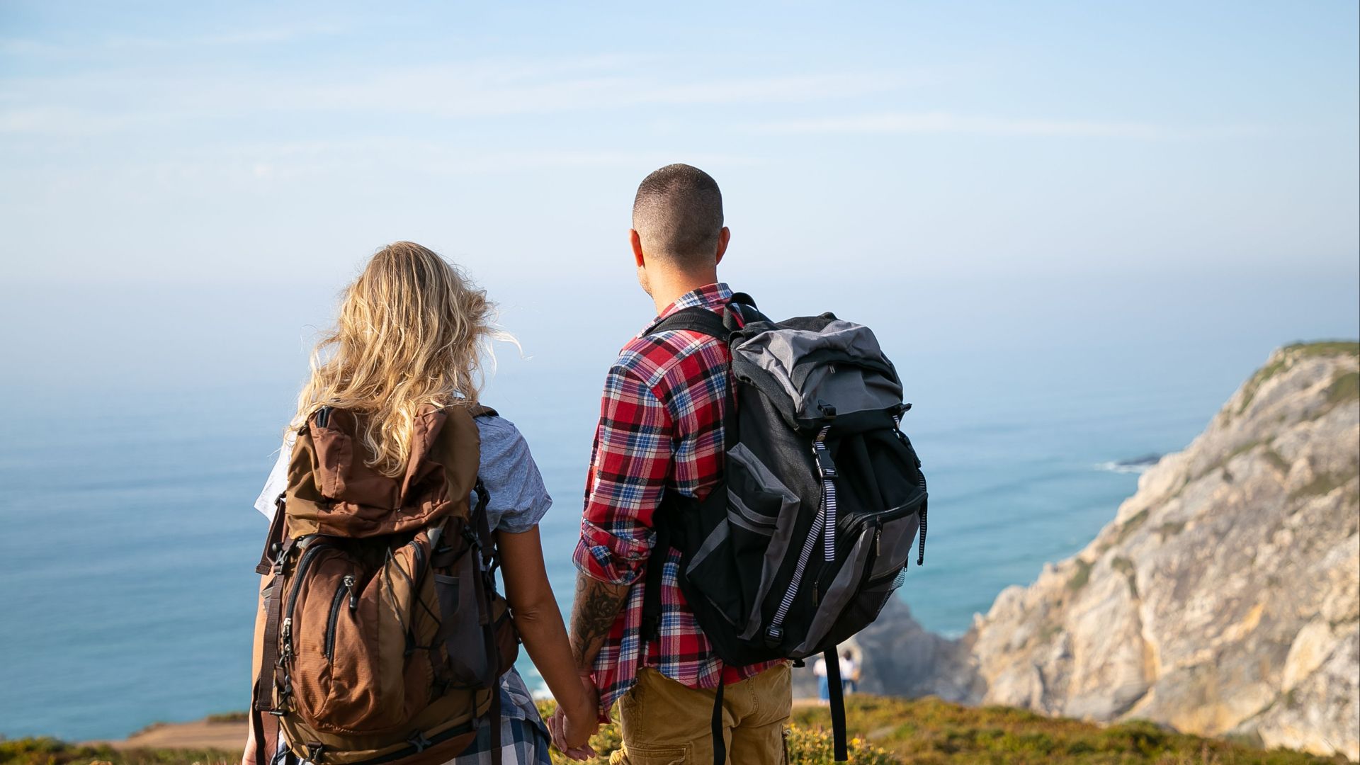 A couple with backpacks holding hands and enjoying the scenic cliffside view in Portugal.