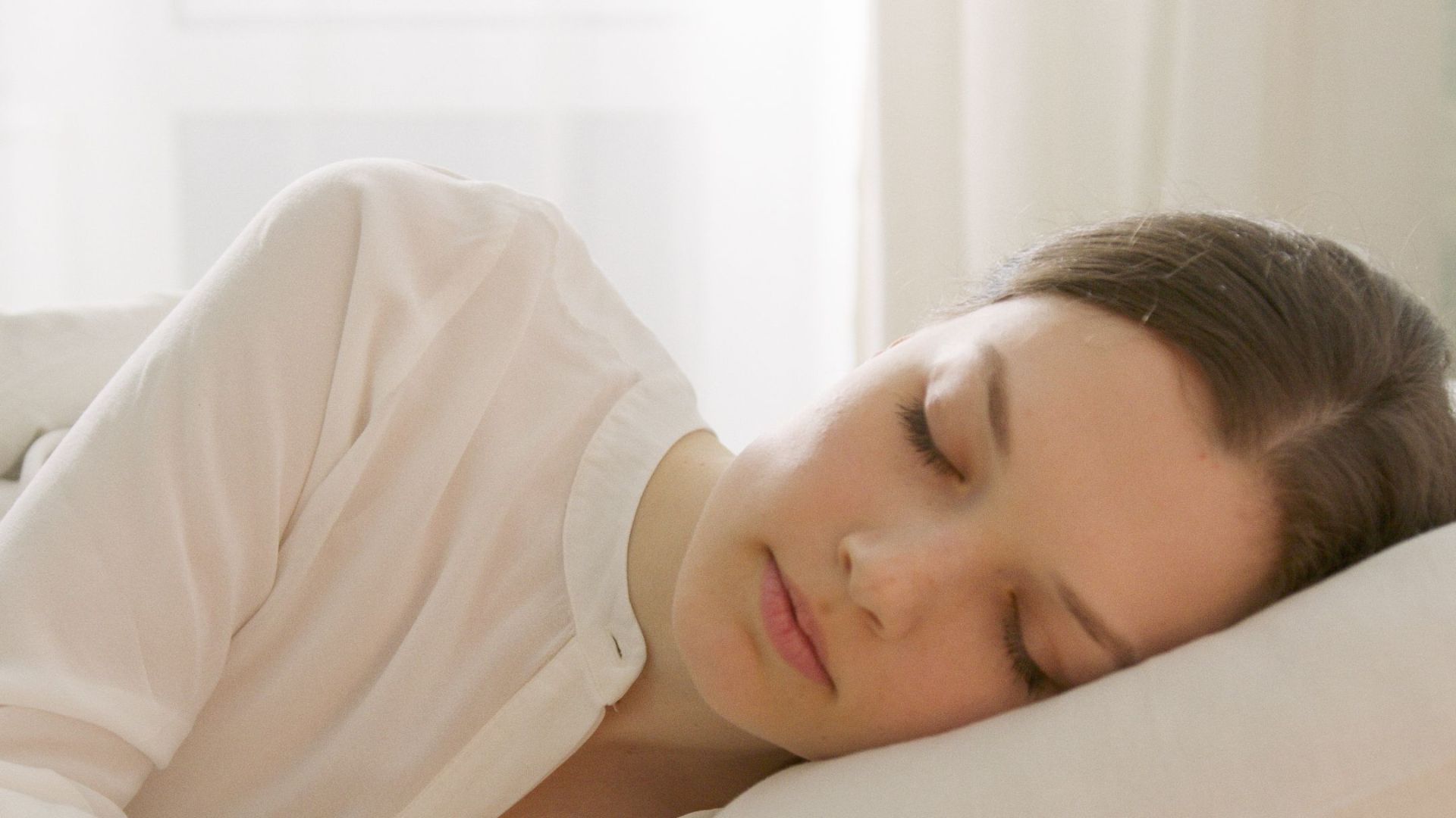 Calm woman sleeping in a white room, reflecting serenity and relaxation, ideal for lifestyle blogs.