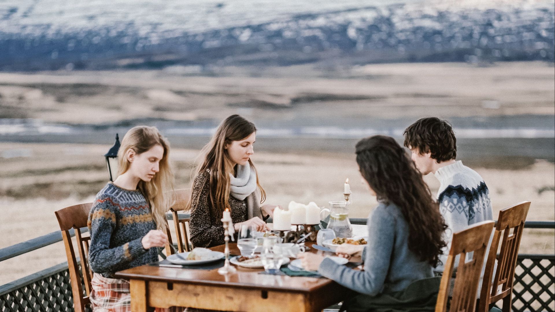 From above group of young tourists in warm clothes having dinner on terrace with beautiful mountain view in Iceland