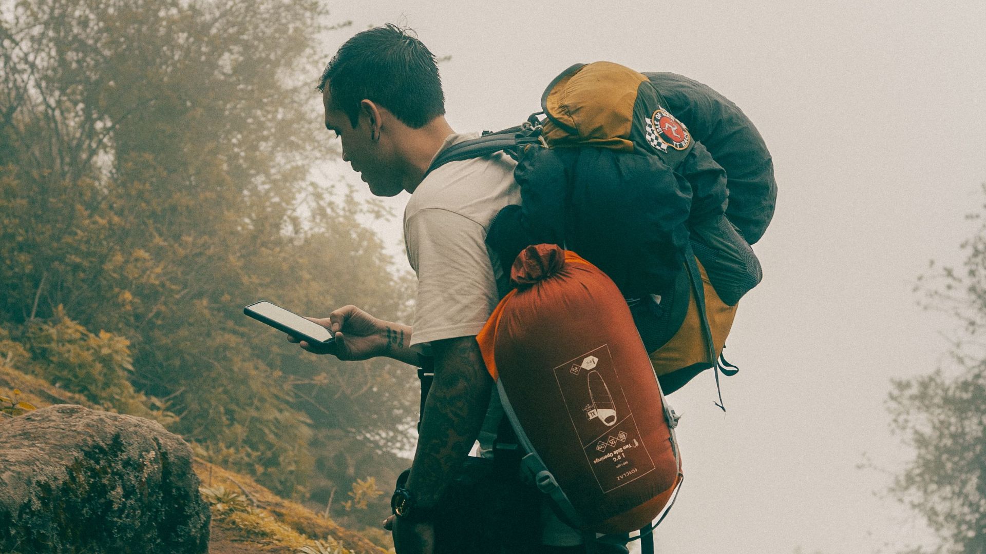 A man hiking uphill in a misty forest, using a smartphone for navigation.