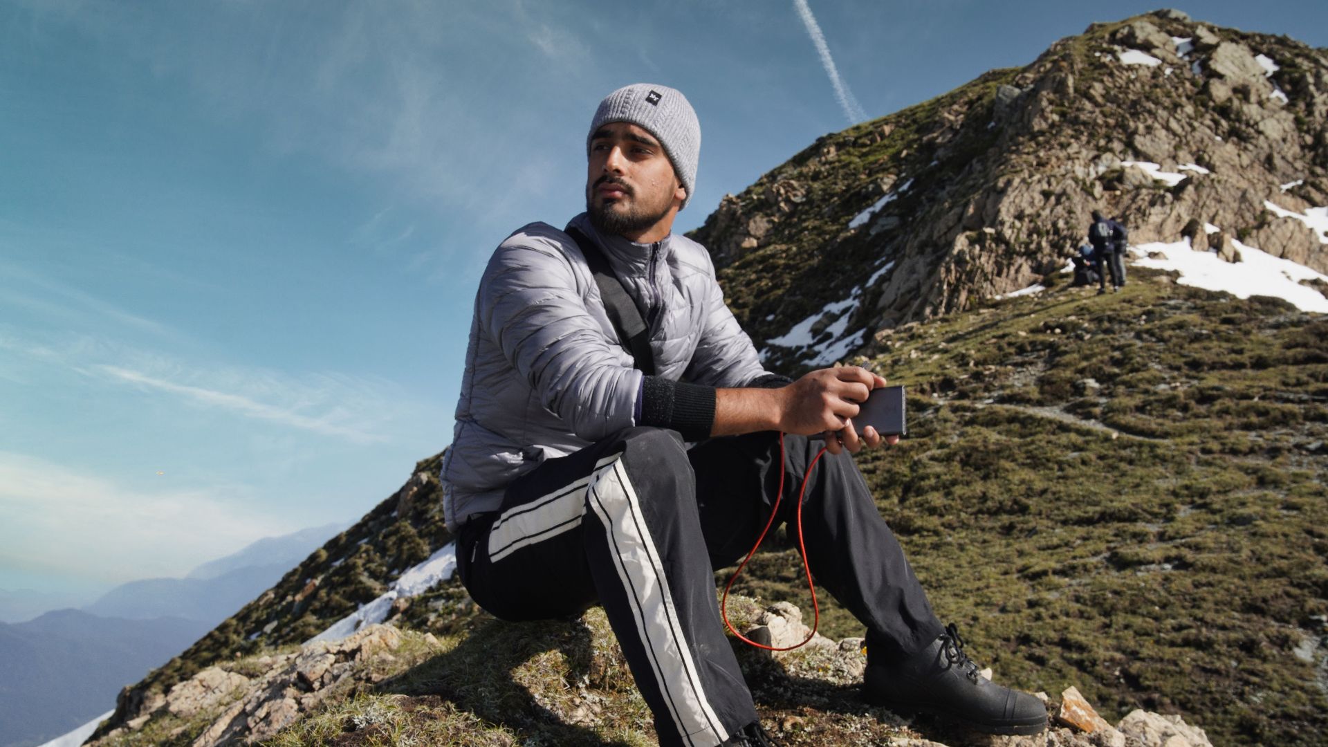 A man sits on a mountain slope in Kashmir, enjoying the scenic view and fresh air.