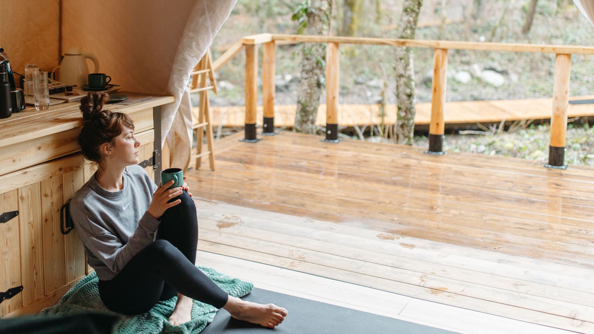 Woman enjoying a warm drink, seated in a cozy glamping tent surrounded by nature.