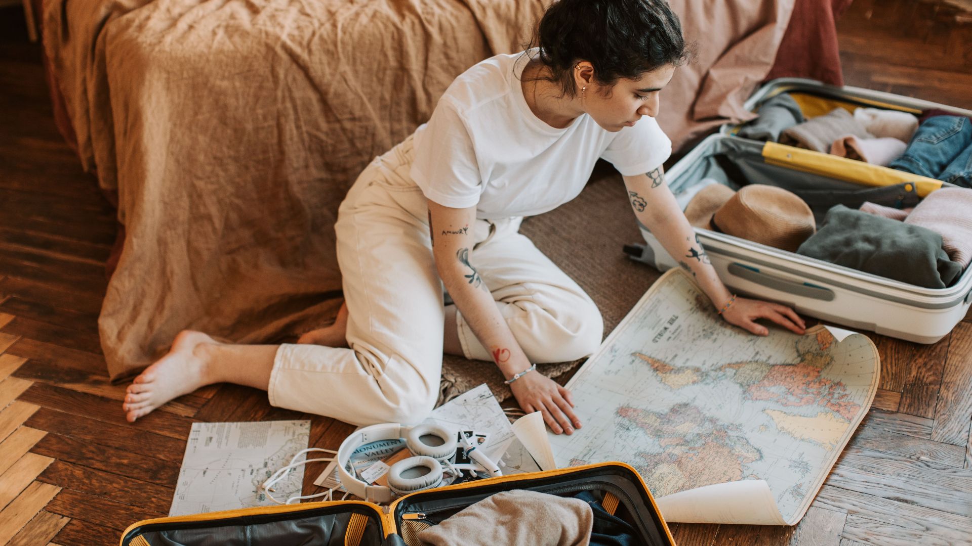 Young woman planning a travel route indoors, surrounded by luggage and a map.