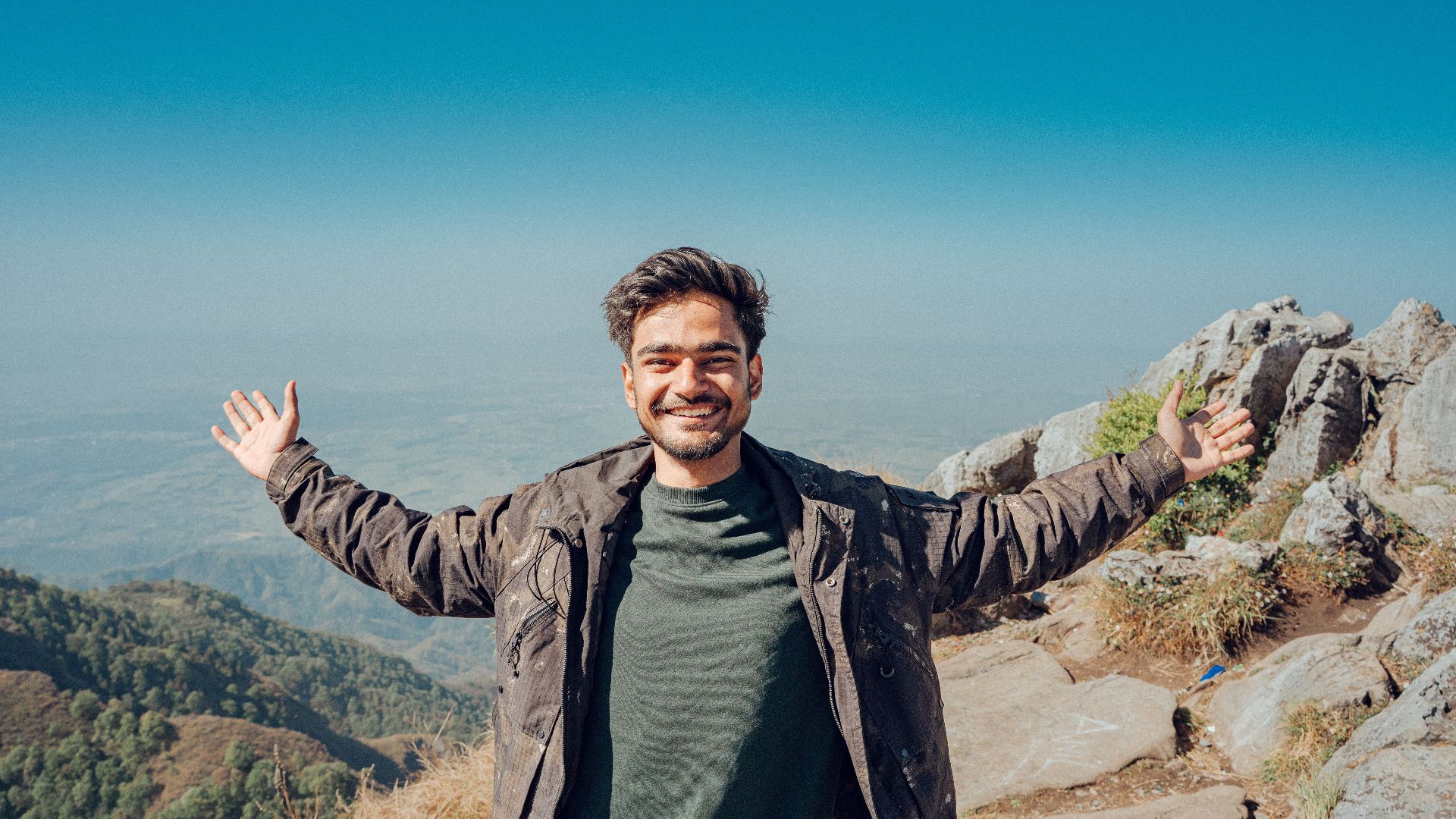 A joyful man stands on a mountain peak with open arms, embracing adventure and nature.