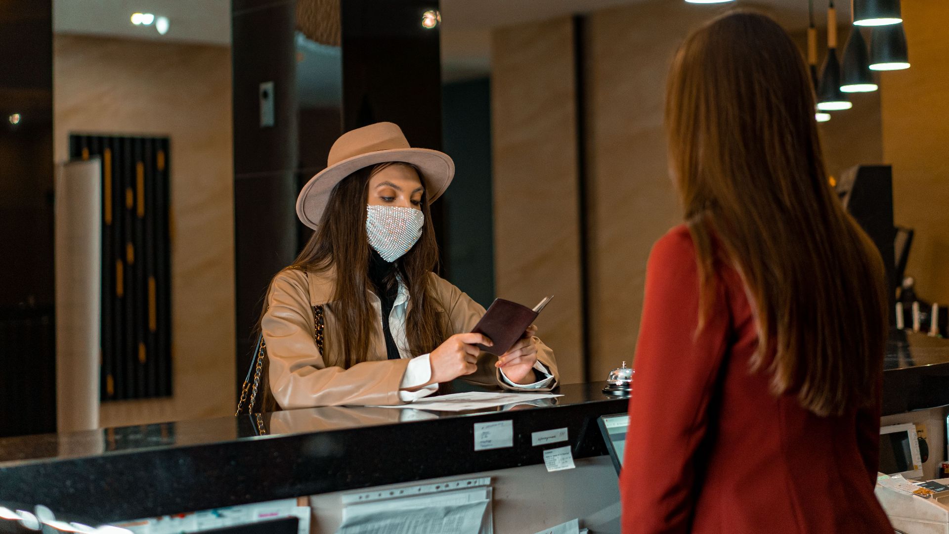 A woman wearing a mask checks in at a hotel reception desk.
