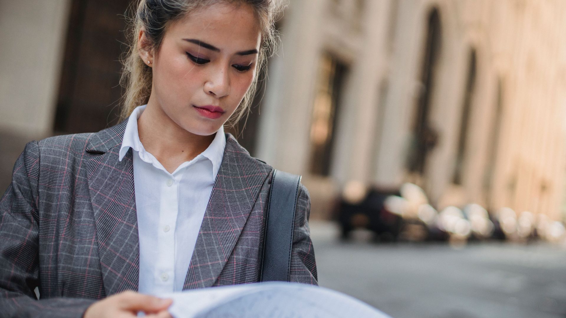Businesswoman in corporate attire reviewing documents on a city street during the day.