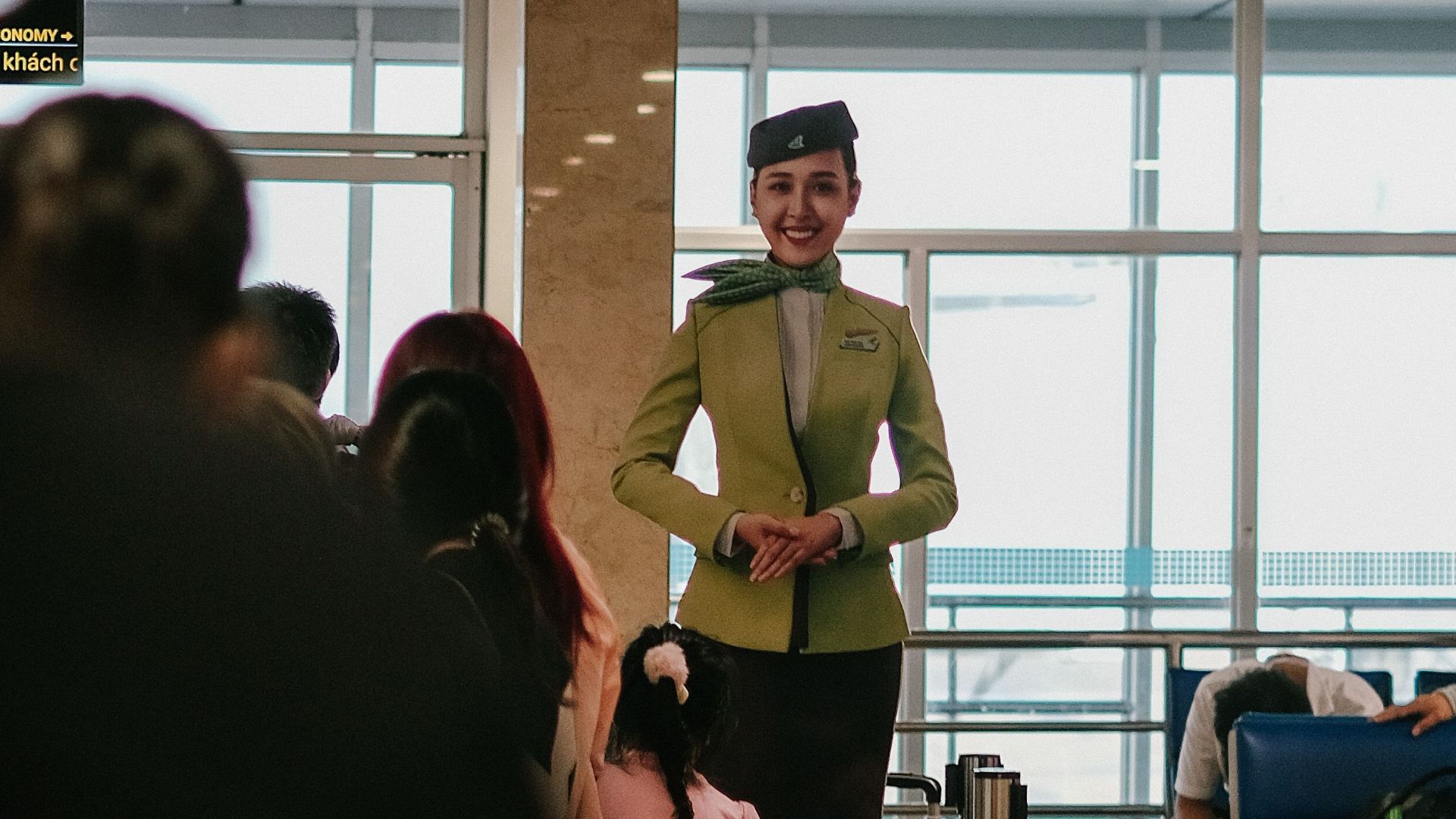 Flight attendant at airport gate 14, Vietnam, offering guidance to passengers indoors.
