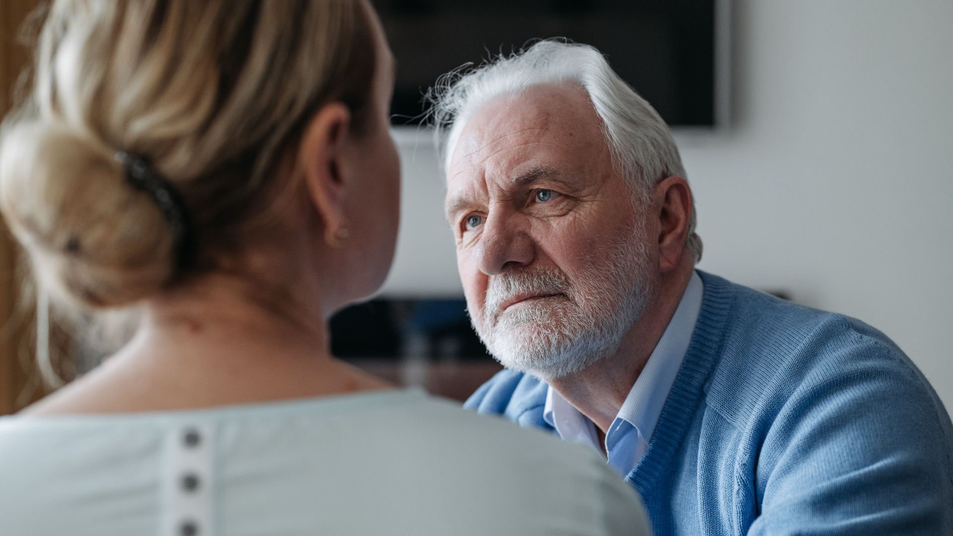 A thoughtful elderly man with grey hair having a conversation indoors, focused on a woman.