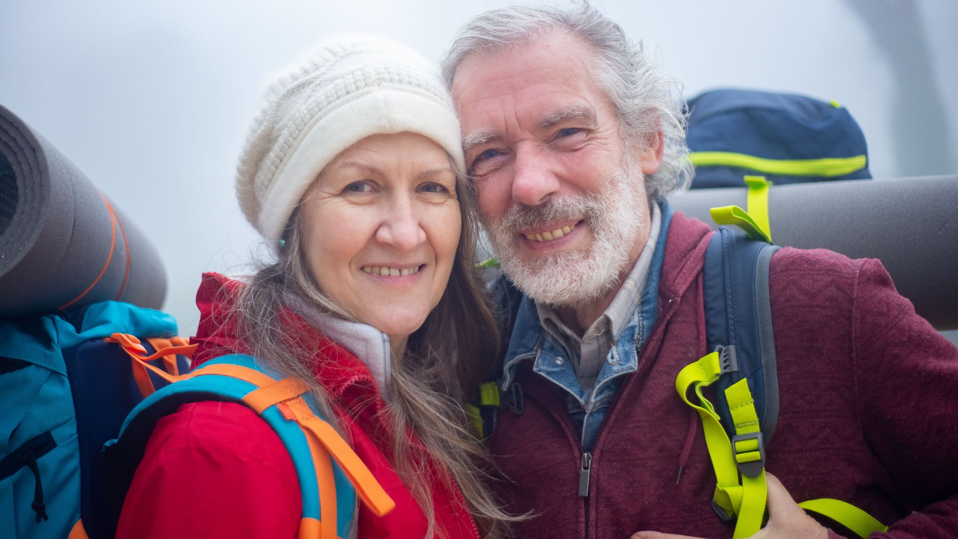 Senior couple hiking with backpacks, smiling in the outdoor misty environment of Portugal.