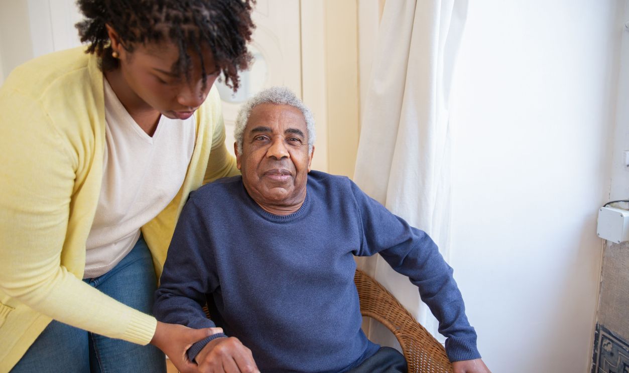 A woman assists an elderly man indoors, focusing on care and support.