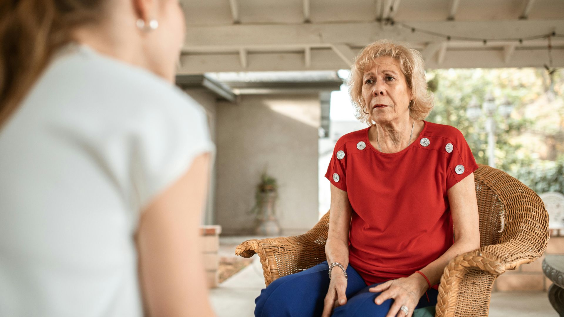 Senior woman in red shirt conversing indoors with younger woman. Daytime scene.