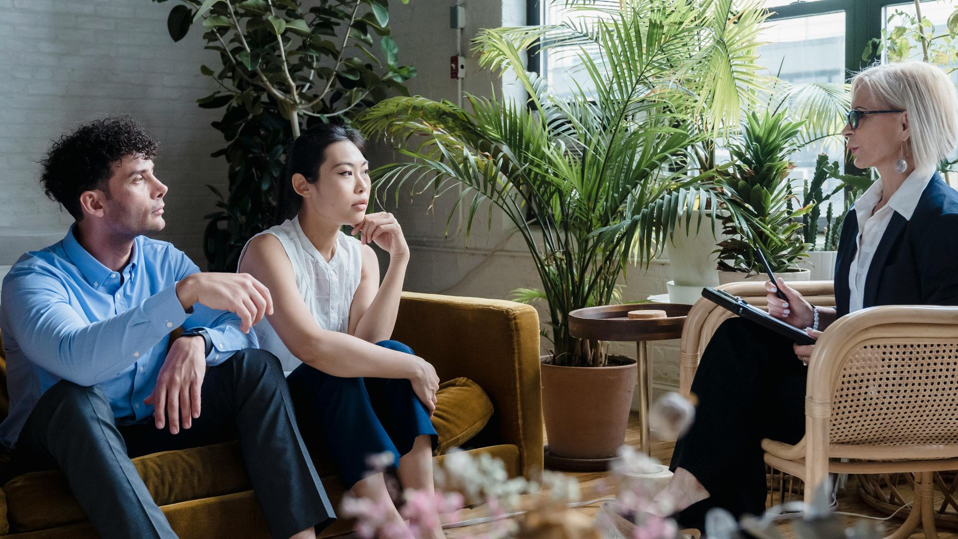 A diverse group engaged in a counseling session in a plant-filled room.
