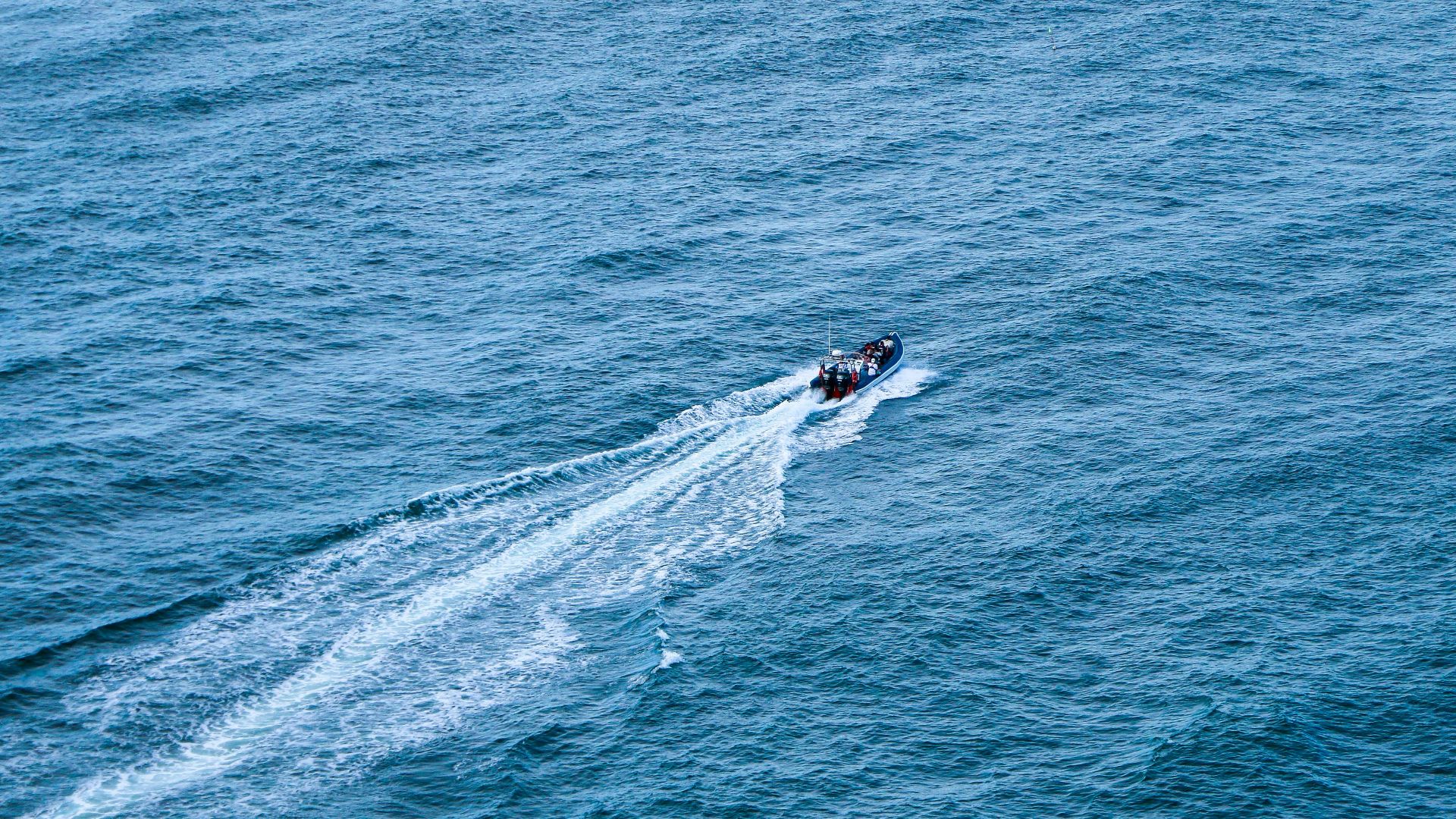 High-angle view of a speedboat slicing through turquoise ocean waters, creating white trails.