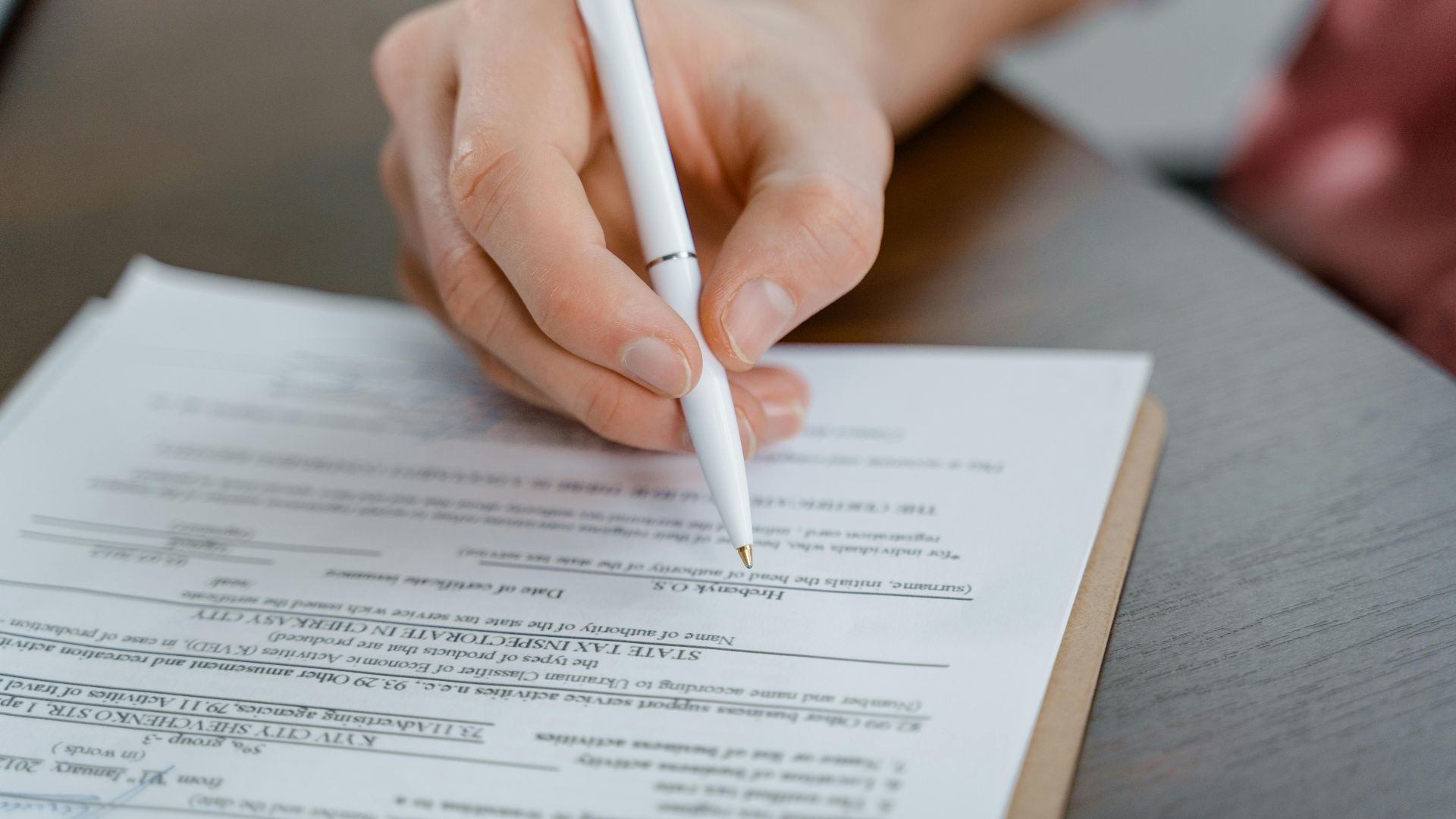 A hand holding a pen signing a document, close-up shot with focus on the paper.