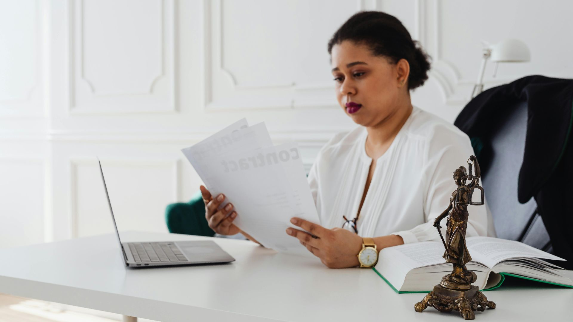 Black woman lawyer reading legal papers at her desk in a modern office.