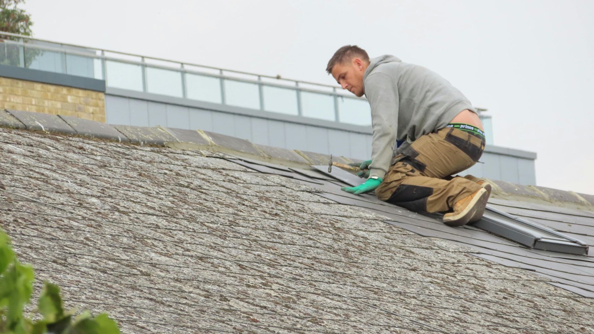 Construction worker installing shingles on a rooftop. Outdoor building maintenance.