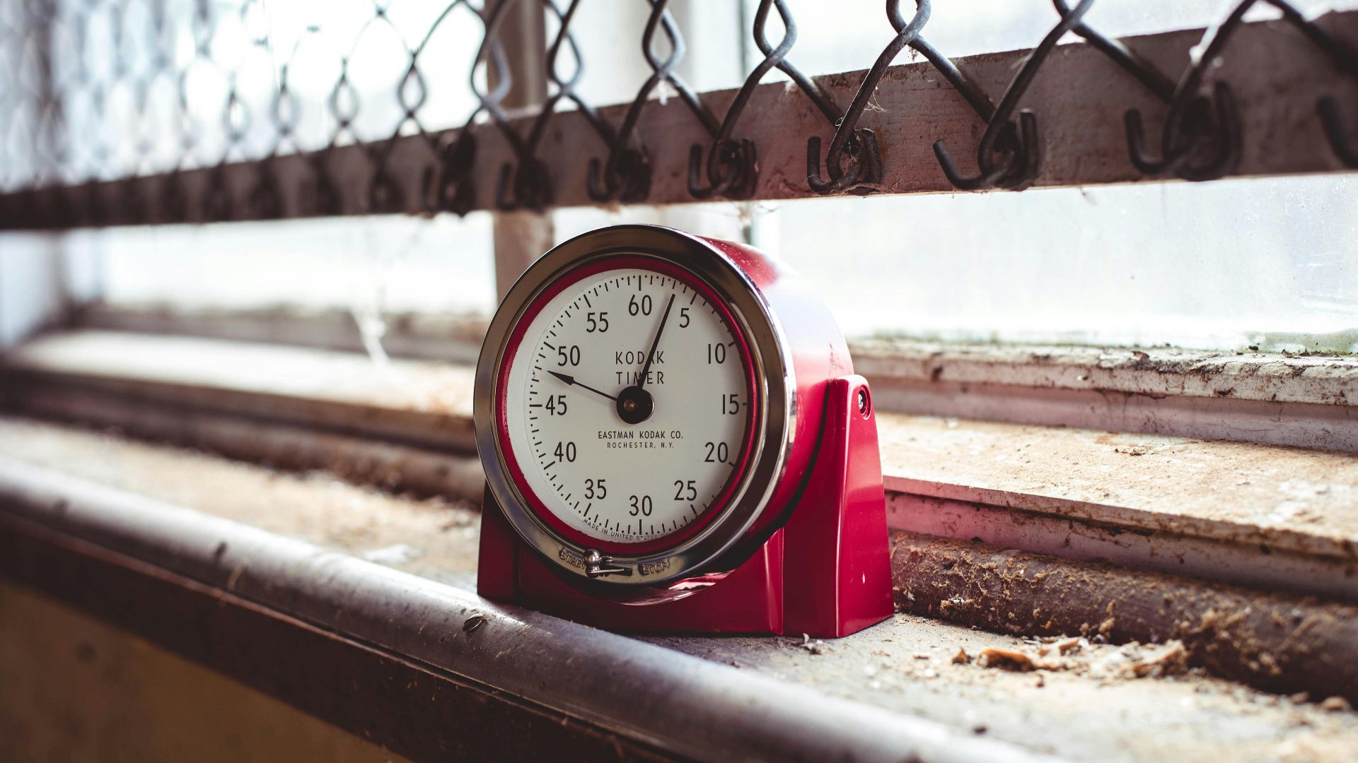 A red timer sits on a dusty windowsill with a chain link fence background, evoking nostalgia.