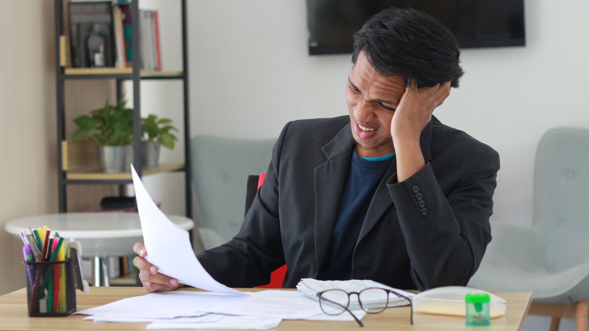A businessman in an office experiencing stress while reviewing documents.