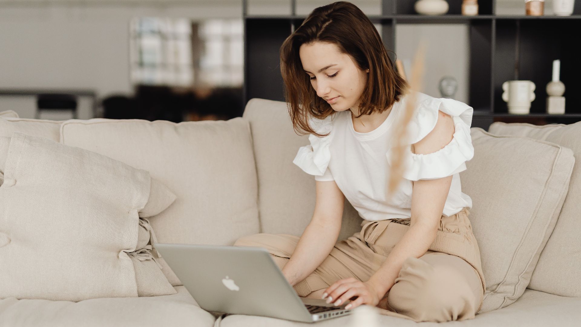 A woman sits on a comfortable couch working on a laptop in a cozy home setting.