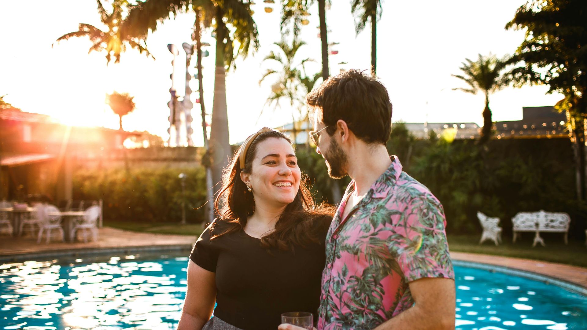 A happy couple smiling by the poolside at sunset, enjoying a romantic summer moment.