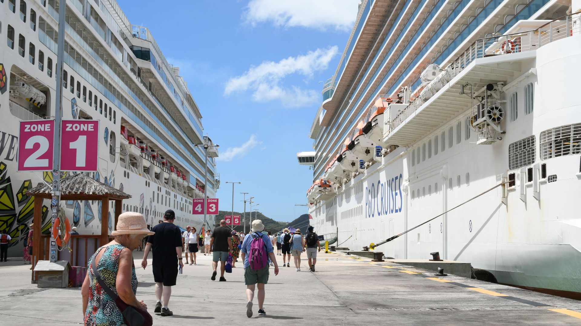 Bustling cruise port with tourists, featuring two large cruise ships under a bright blue sky.