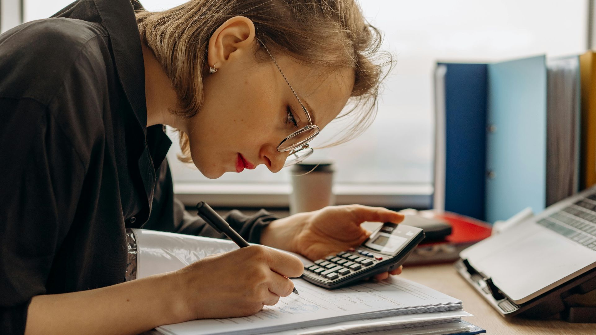 Young woman diligently working on accounting with a calculator and documents. Perfect for business and finance themes.