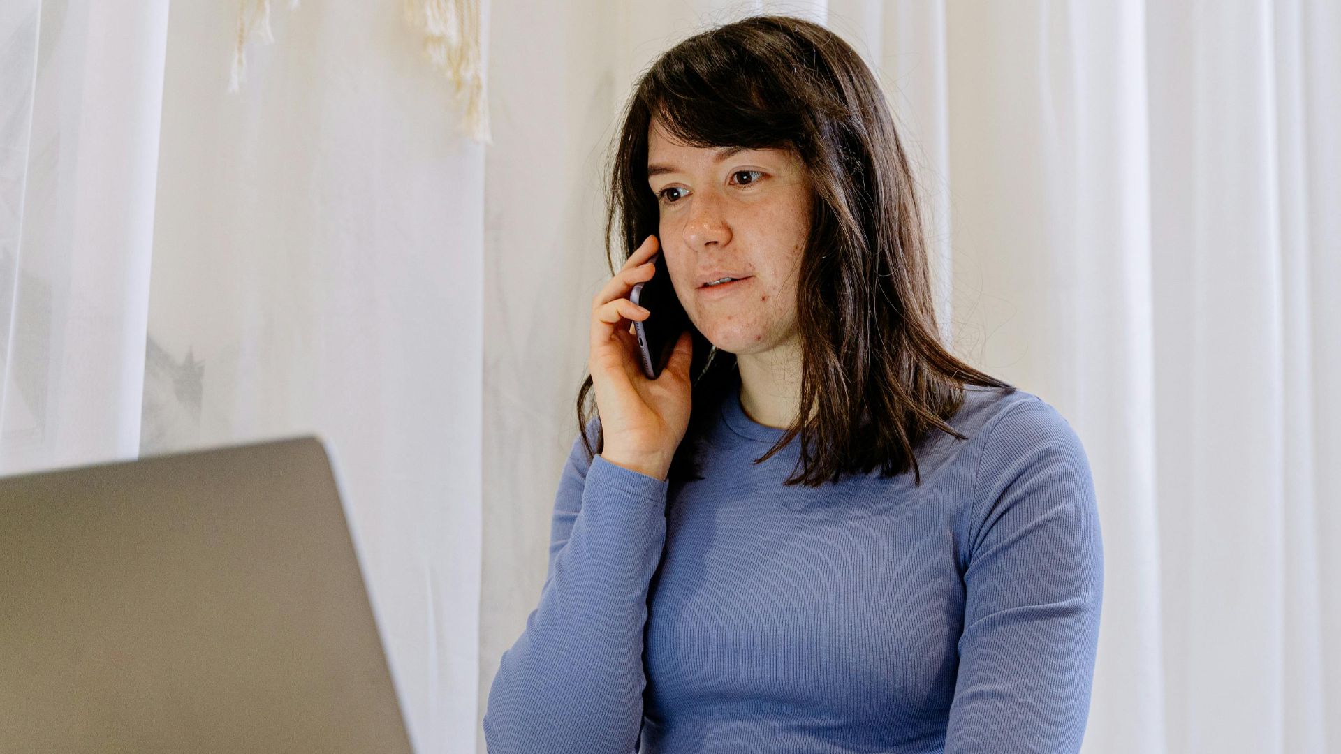 Young woman multitasking with a smartphone and laptop in a cozy indoor setting.