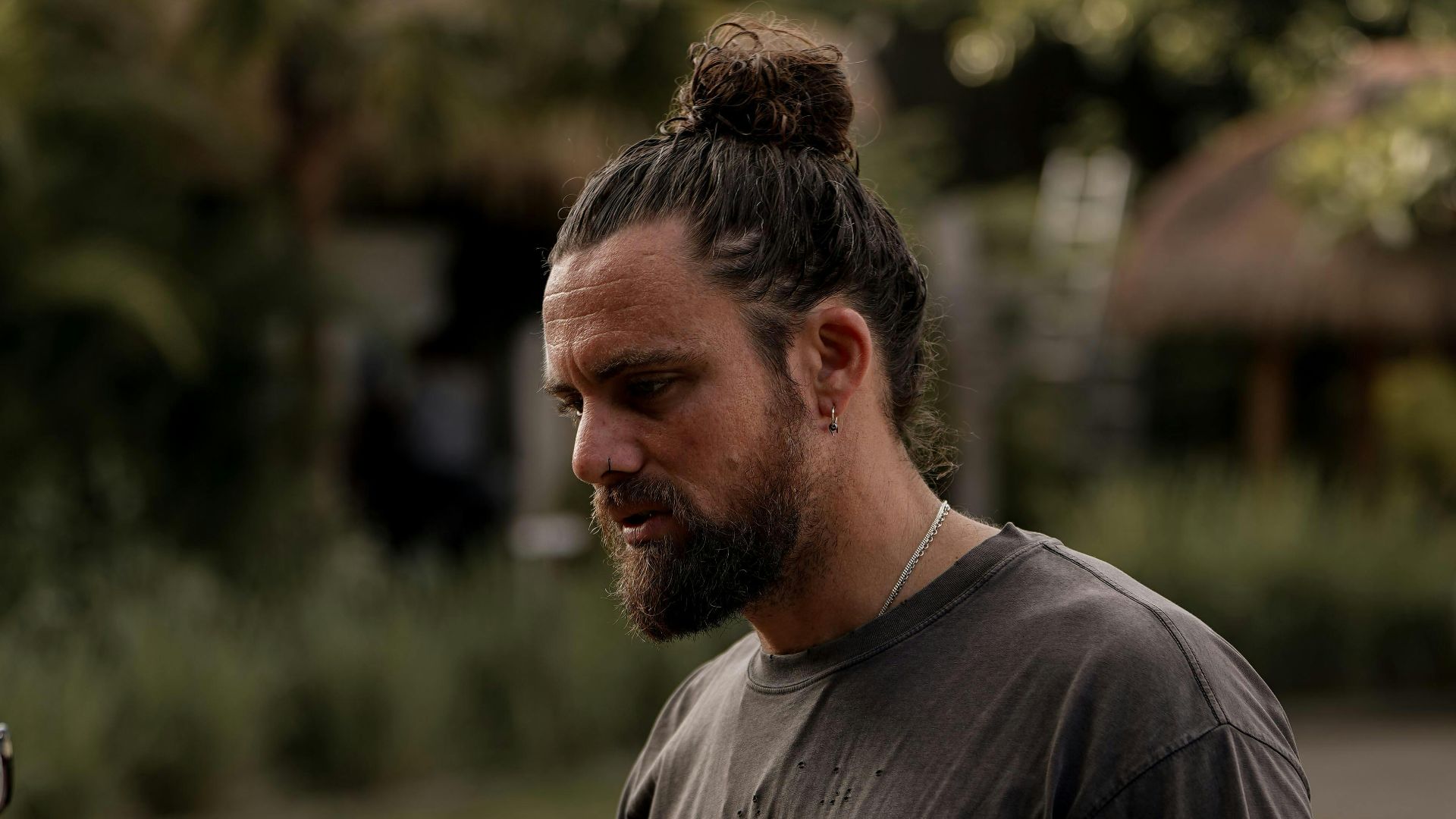 Man with bun hairstyle engaged in conversation outdoors in natural light setting.