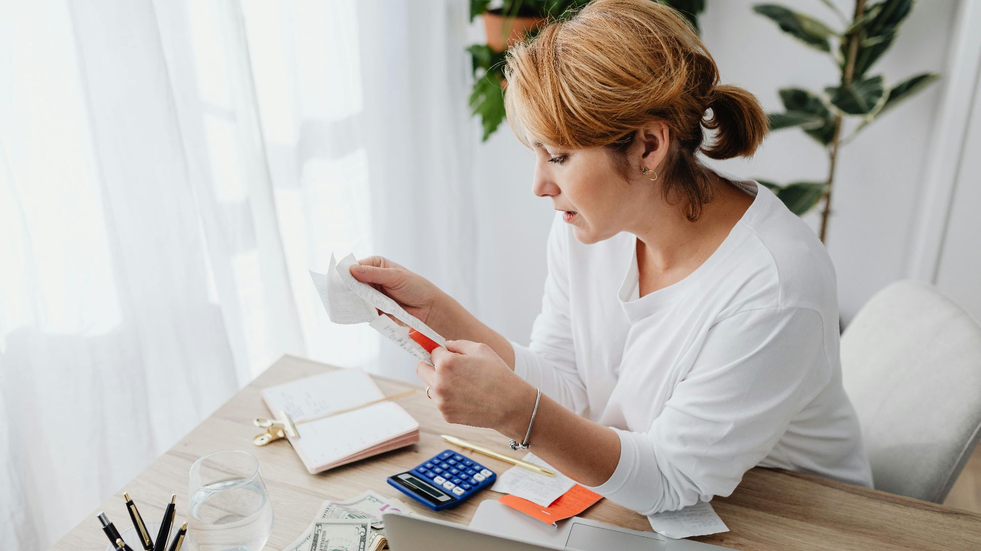 Woman sitting at a desk managing finances with a calculator and paper receipts in an office setting.