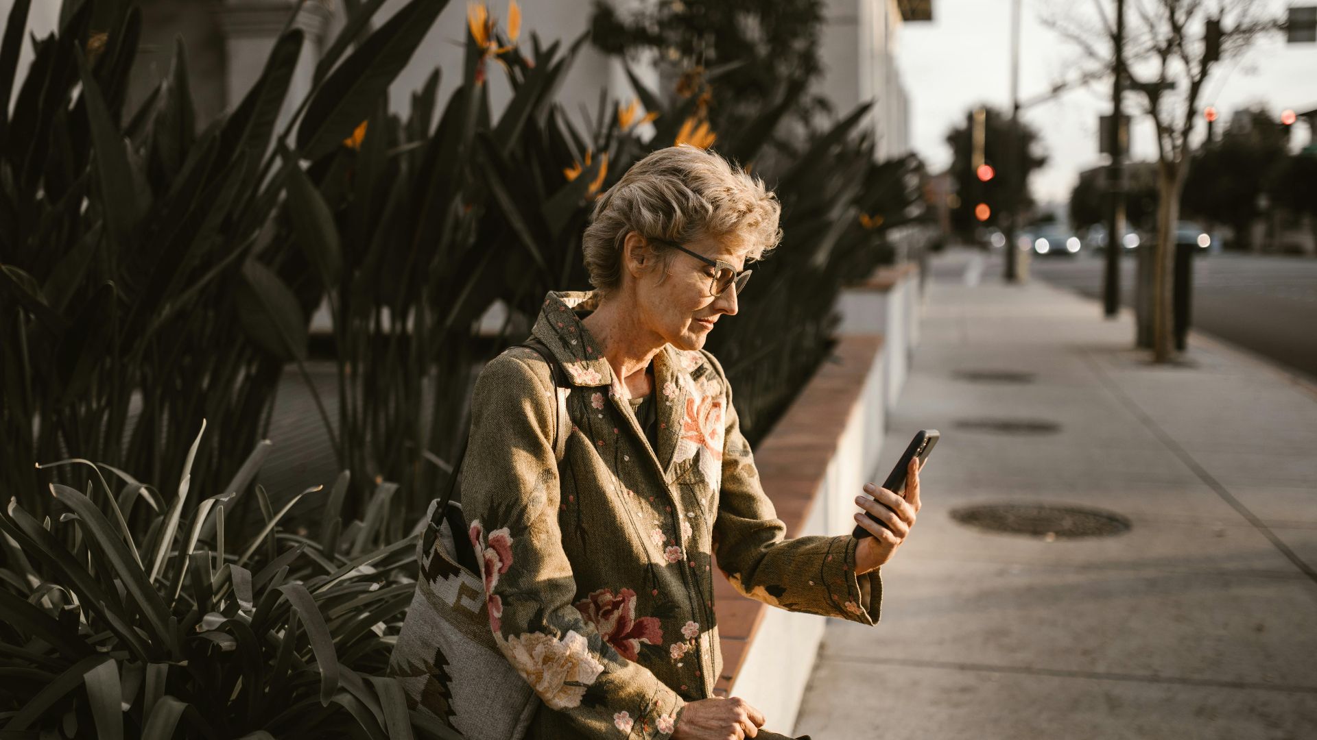 Senior woman sitting outdoors with smartphone, embracing technology in a city setting.