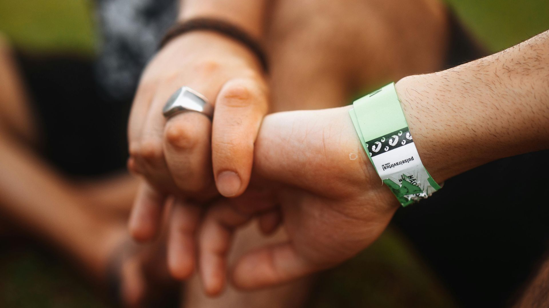 A detailed close-up of two hands clasped together, featuring a wristband, outdoors.