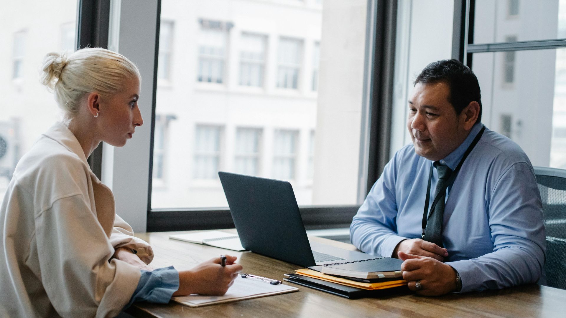 Ethnic boss asking question to female candidate filling information form on clipboard during hiring meeting