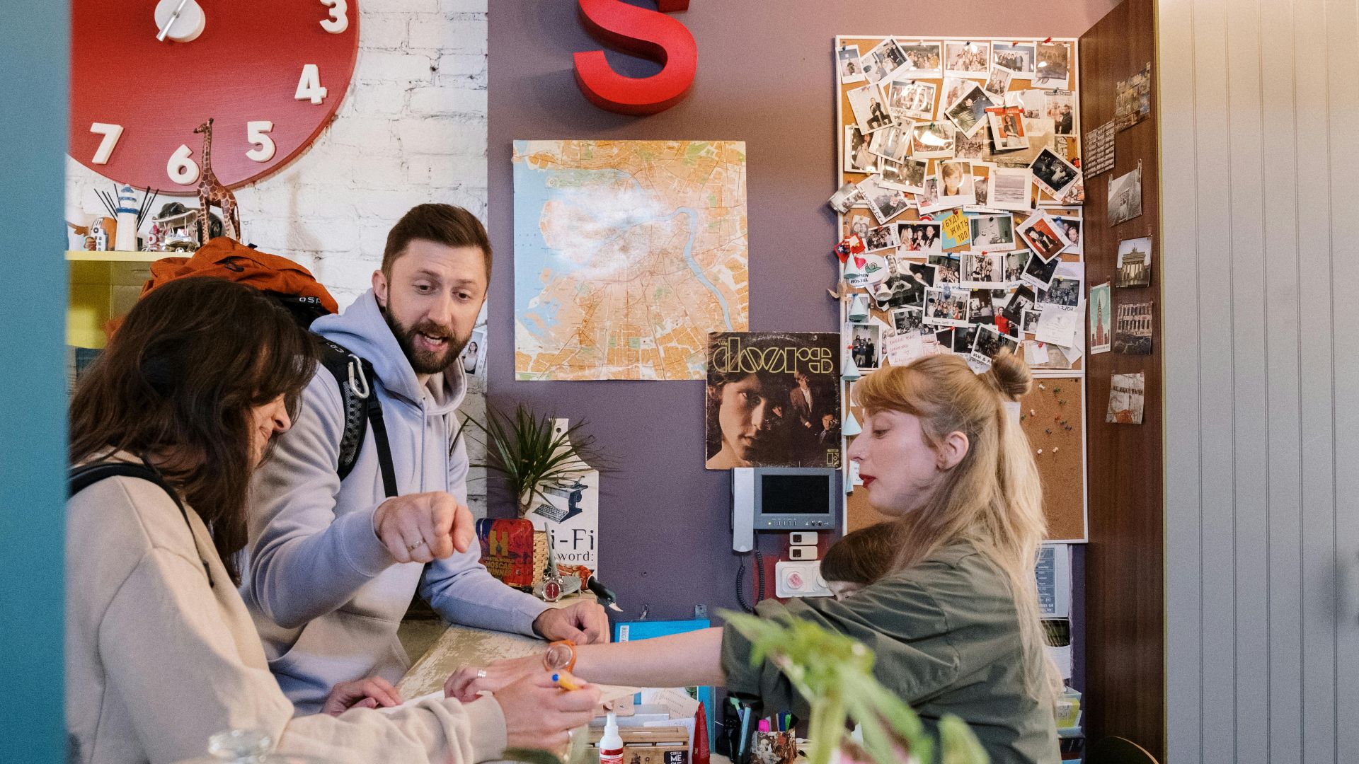 Guests checking in at a hostel reception with a warm interaction between a couple and staff.