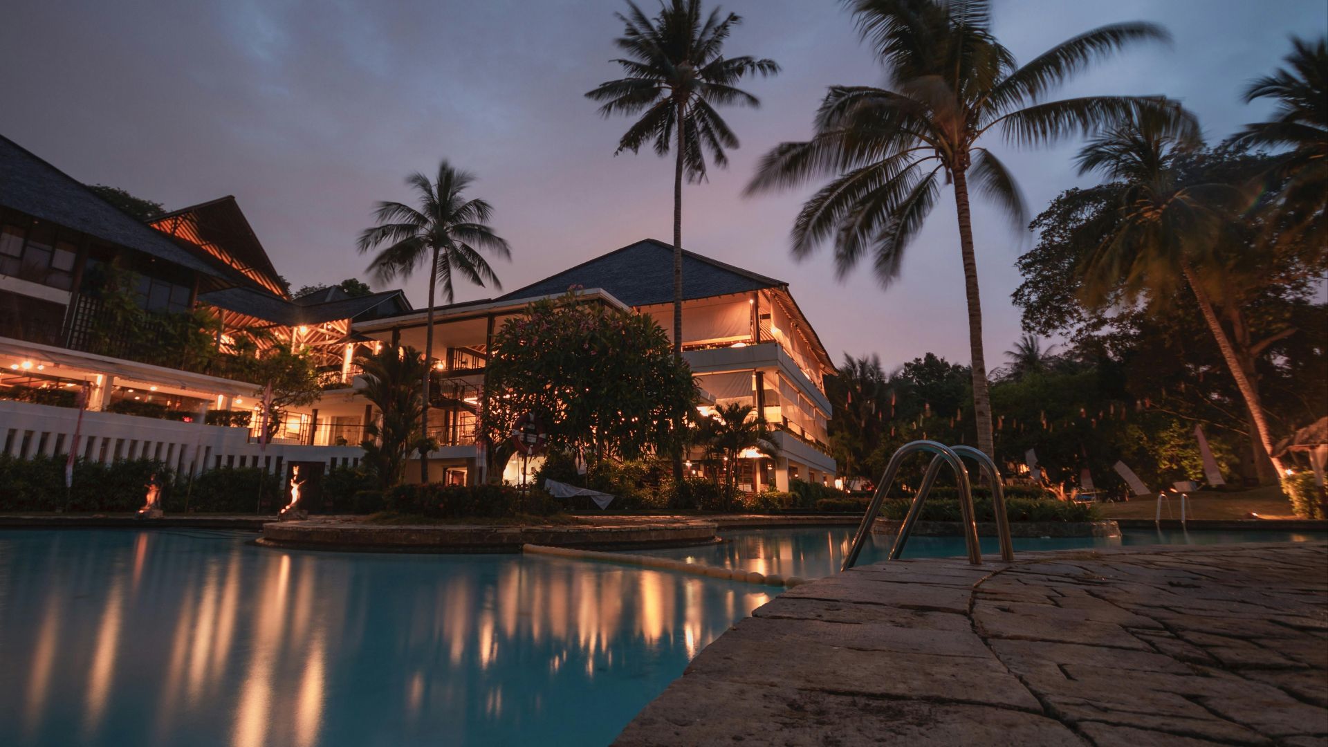Luxurious tropical resort with swimming pool and palms at dusk, perfect for a tranquil vacation.