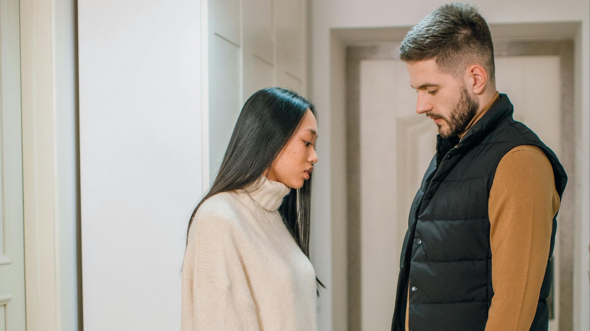 A couple stands indoors, engaged in a thoughtful conversation, expressing relationship dynamics.