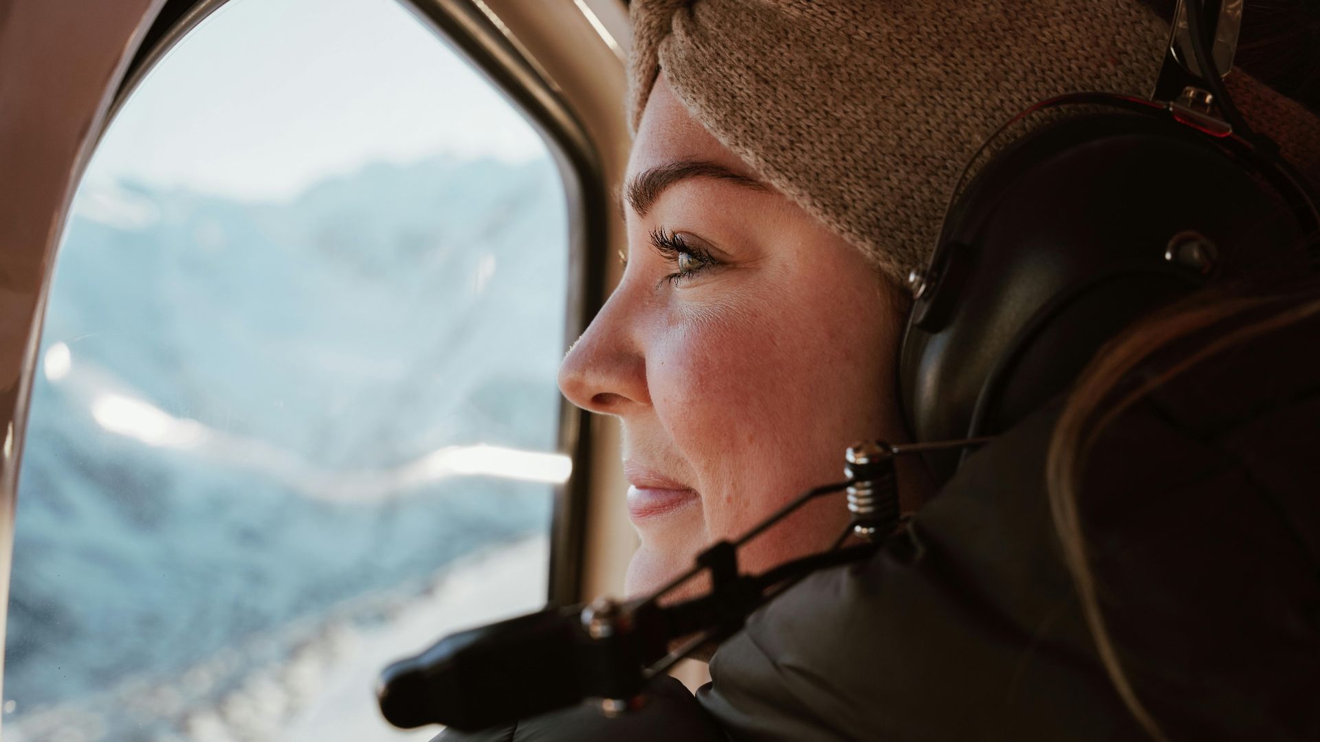 A woman enjoys a helicopter view of Canterbury's snowy mountains during winter.