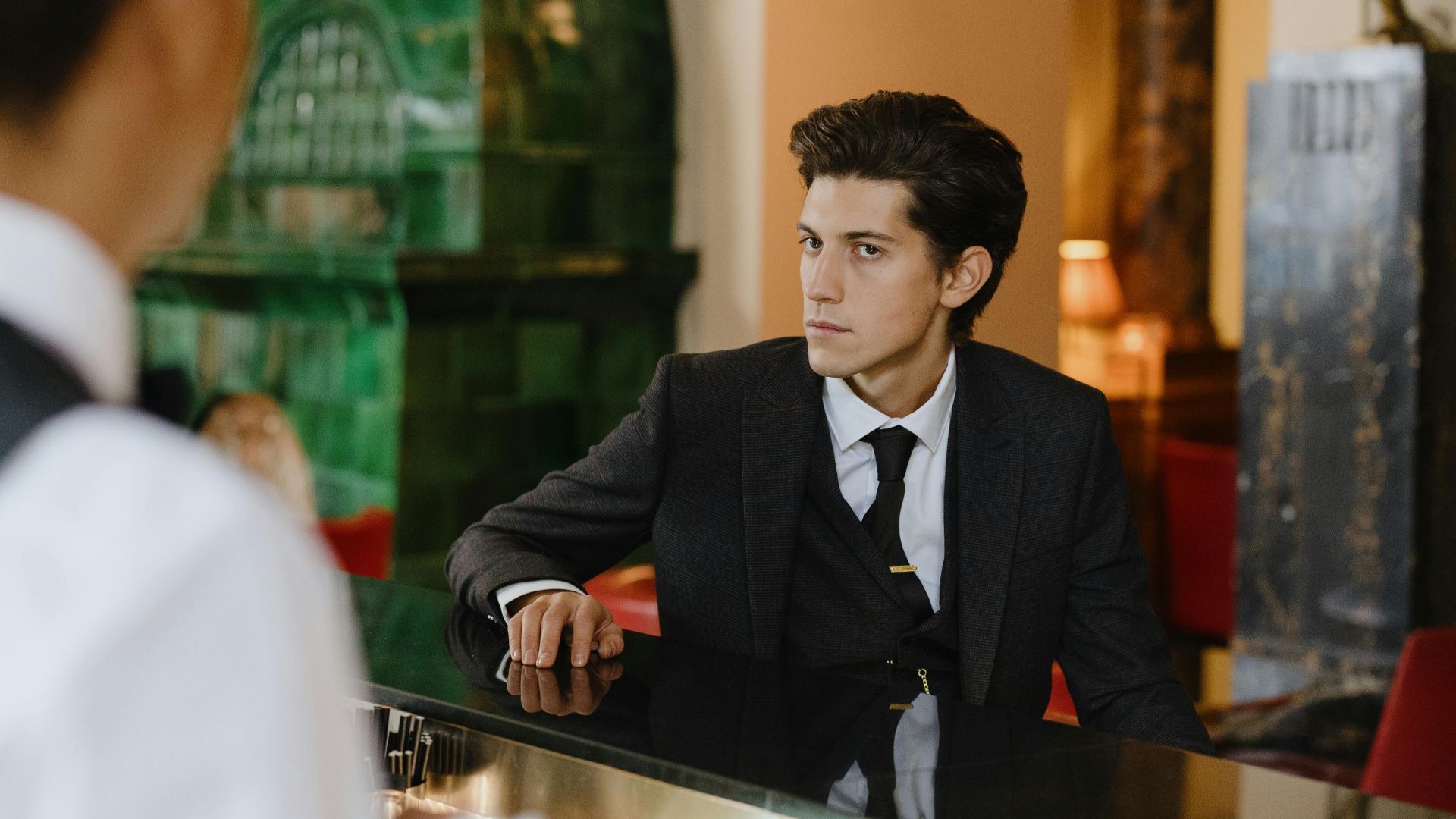 Sophisticated man in a suit sitting at a vintage bar counter indoors, exuding elegance and style.