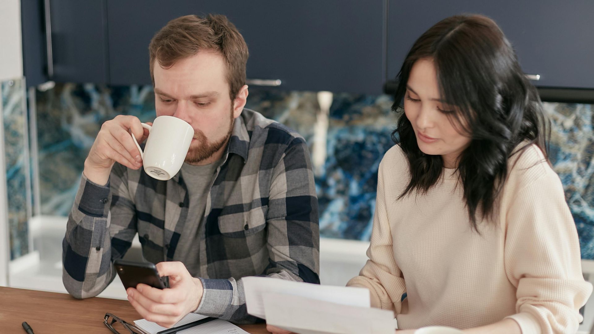 A couple reviewing bills, using a calculator and smartphone, in a modern kitchen.