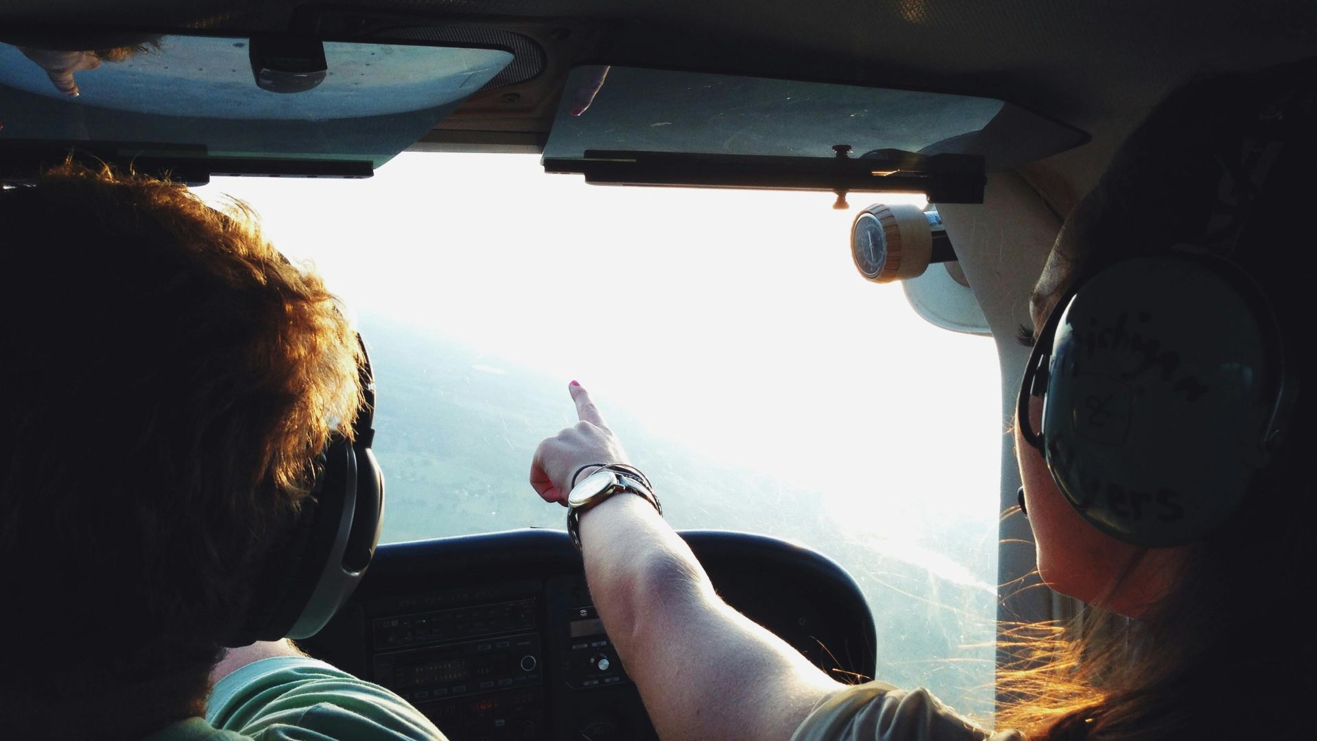 Two people in a small aircraft cockpit, navigating with headsets during a daytime flight.