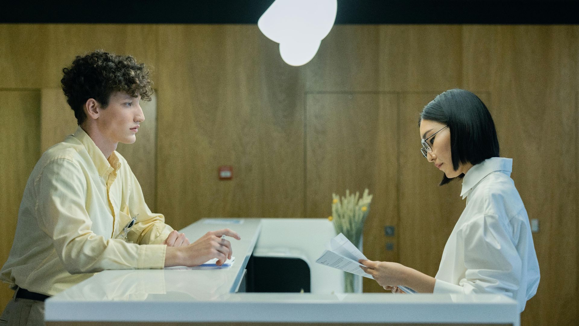 A young man and woman interacting at a modern office reception desk indoors.