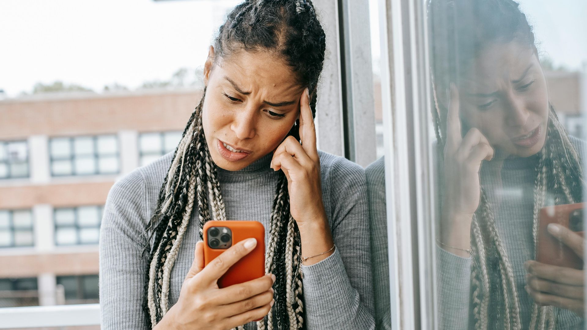 Unhappy African American female standing on balcony while holding smartphone and looking at screen