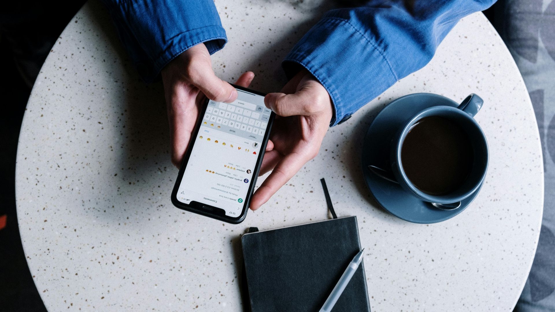 Person using smartphone at table with notebook and coffee, ideal for tech and lifestyle themes.