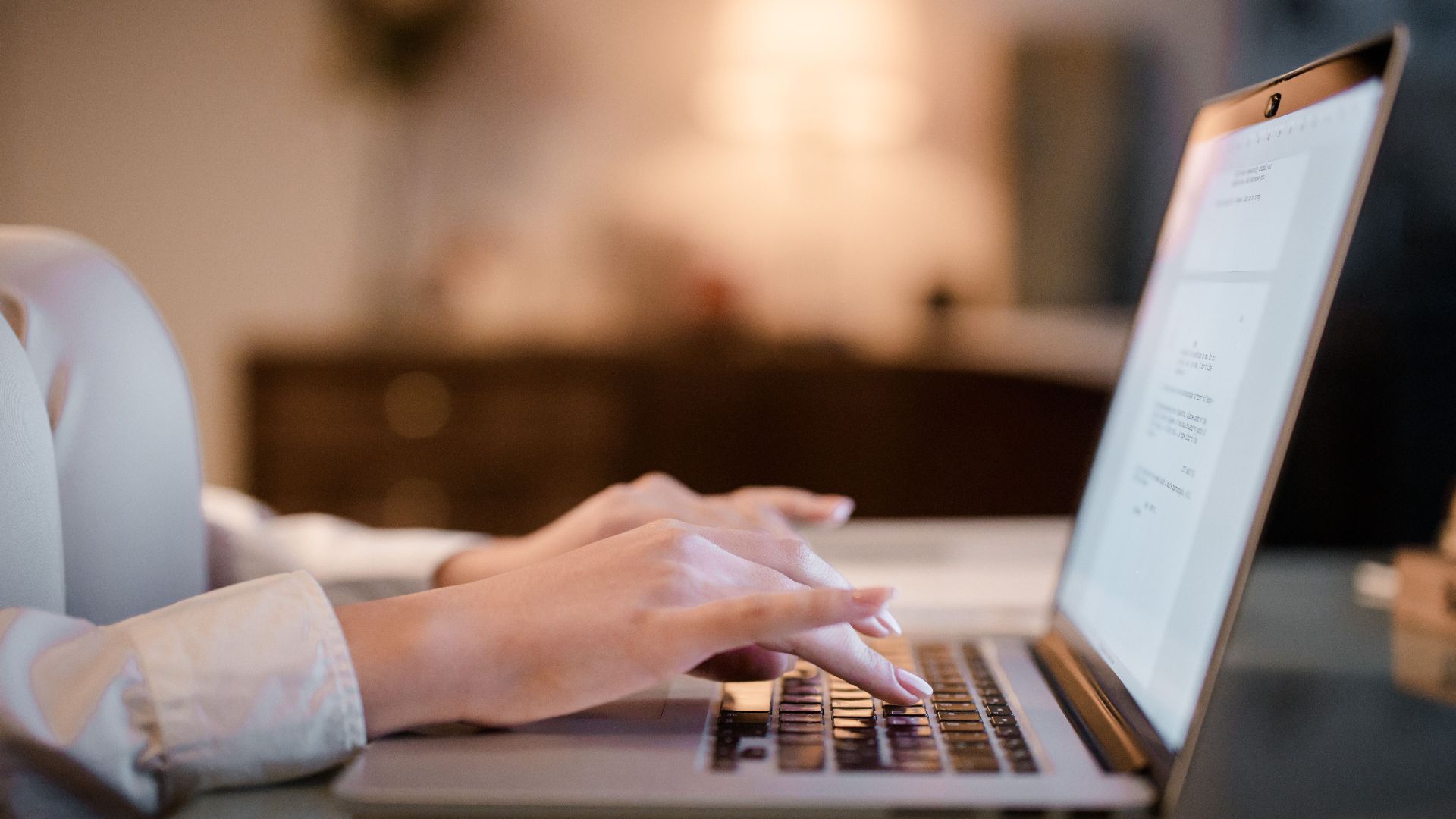Close-up of hands typing on a laptop at home, showcasing a cozy work environment.