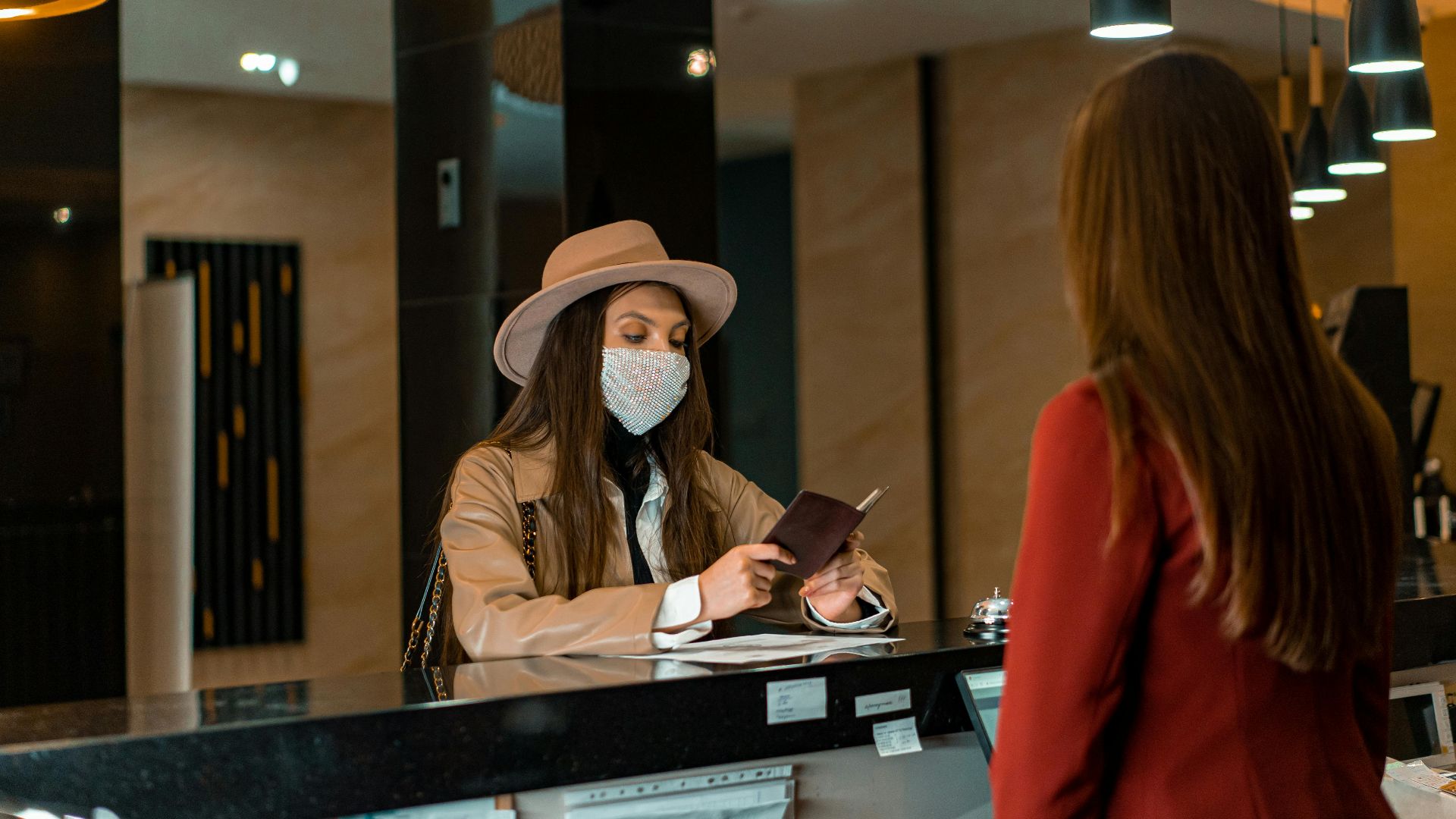 A woman wearing a mask checks in at a hotel reception desk.