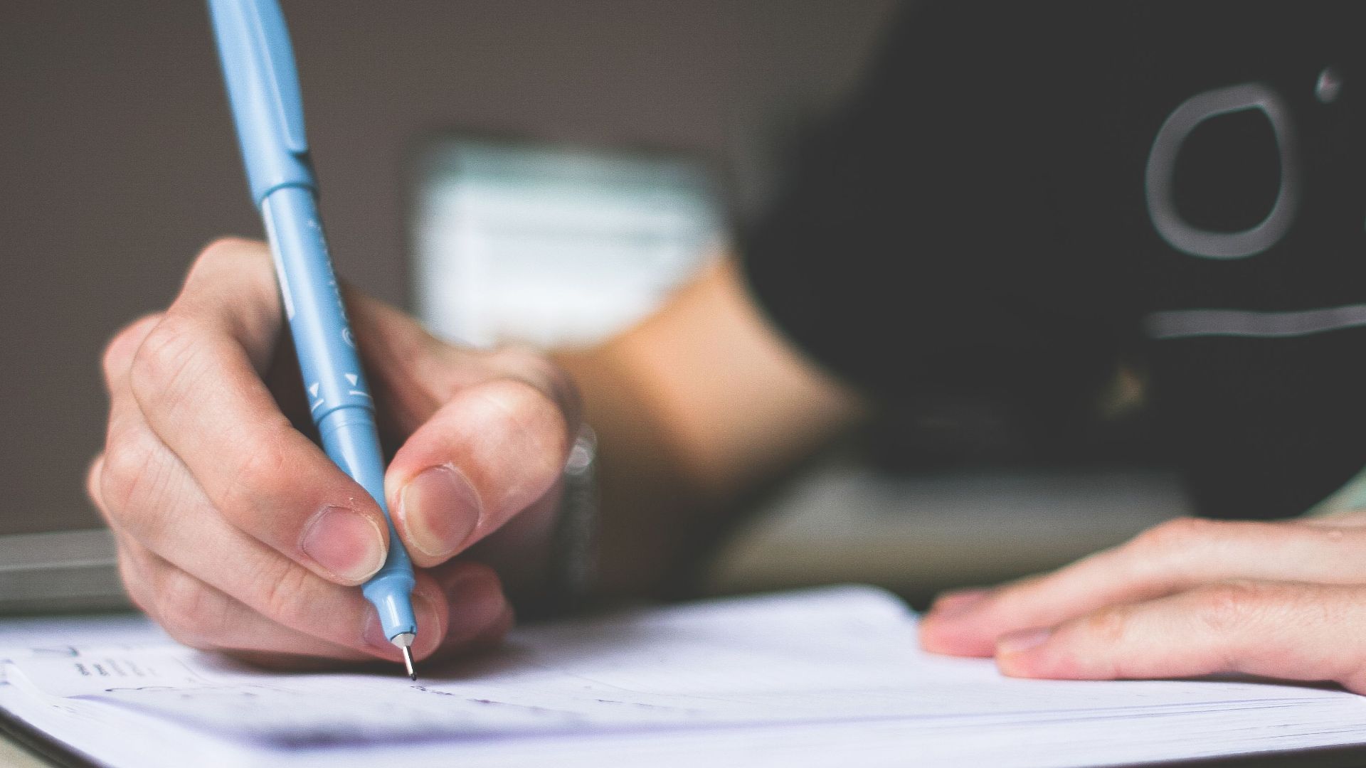 Close-up of hand writing in notebook using a blue pen, focus on creativity.