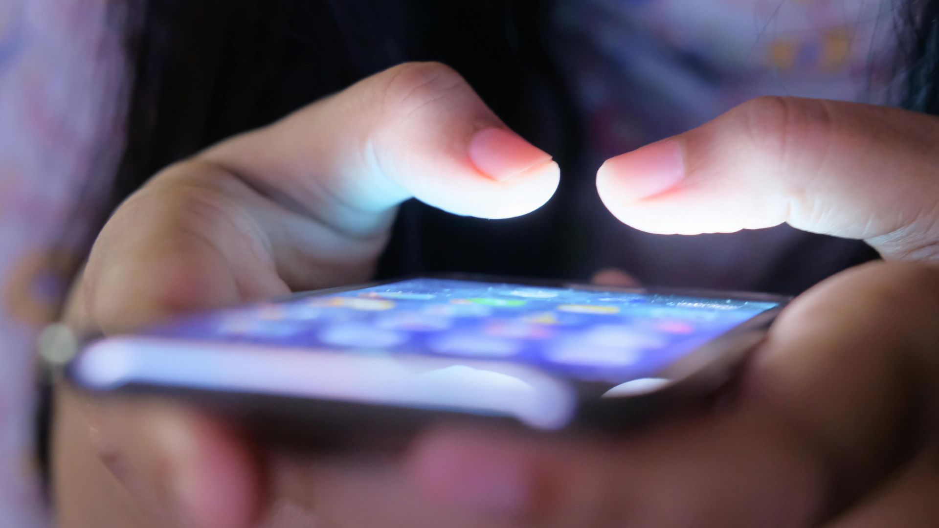 A close-up shot of hands holding a smartphone in low light, showcasing a glowing screen.