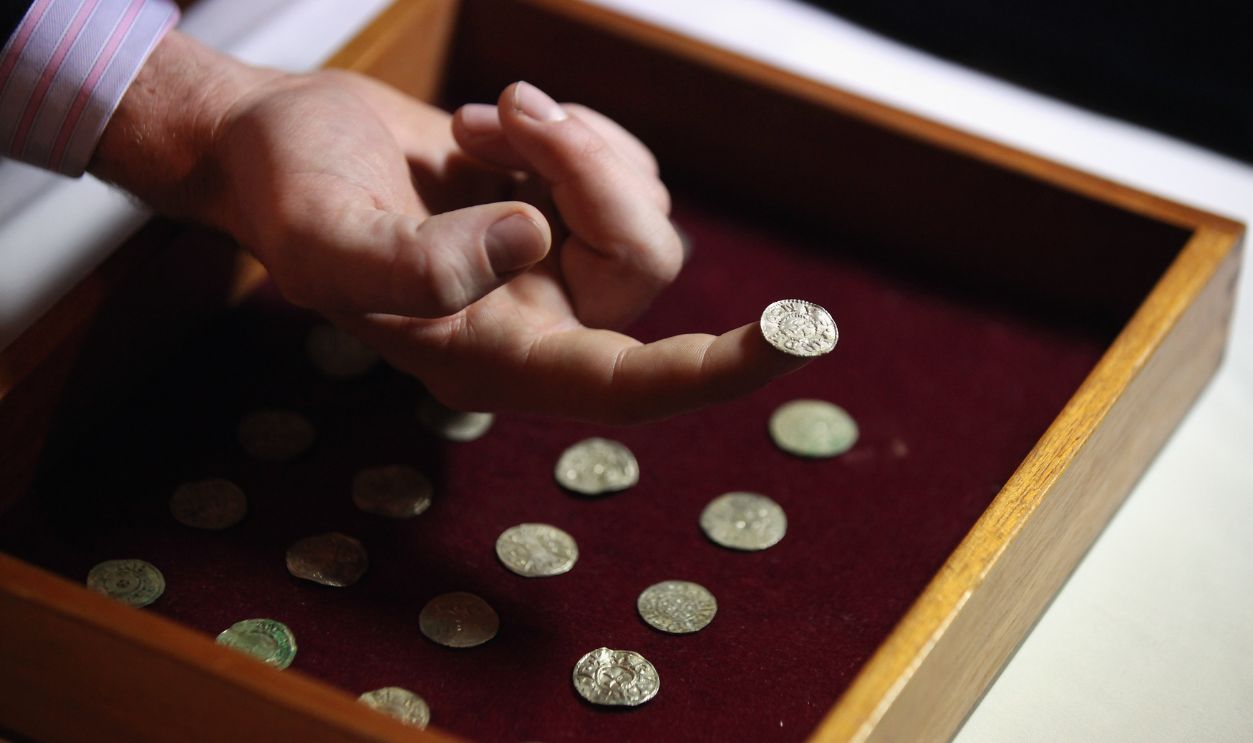 Getty Images - 135777674 - An employee of the British Museum examines a silver coin dating from 900 AD which is part of the Silverdale Viking Hoard on December 14, 2011 in London, England. The hoard, which was discovered by local metal-detectorist Darren Webster in North Lancashire, comprises of 201 silver objects including arm-rings, coins, finger-rings, ingots, brooch fragments and fine wire braid.